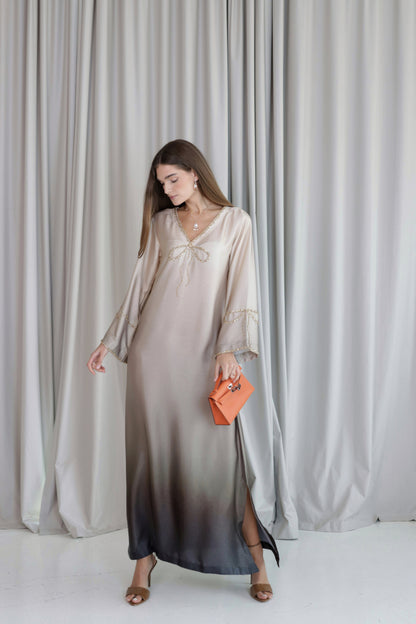 Woman wearing a long, light-colored dress with an ombre effect against a plain background.